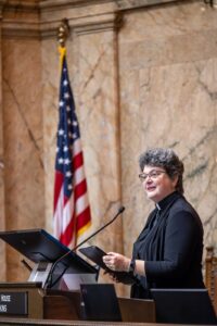Rev. Mary, wearing a clerical collar, delivering a blessing at the Washington State House of Representatives