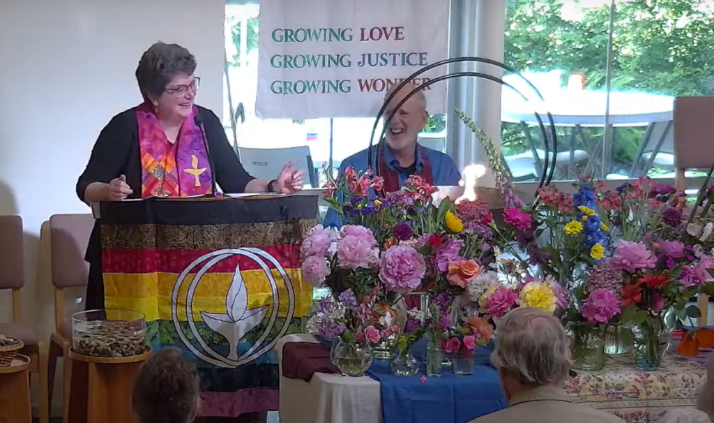 Rev. Mary laughing at the pulpit on Flower Communion Sunday as she tells the story of how she learned the real meaning of the song Run Mary Run