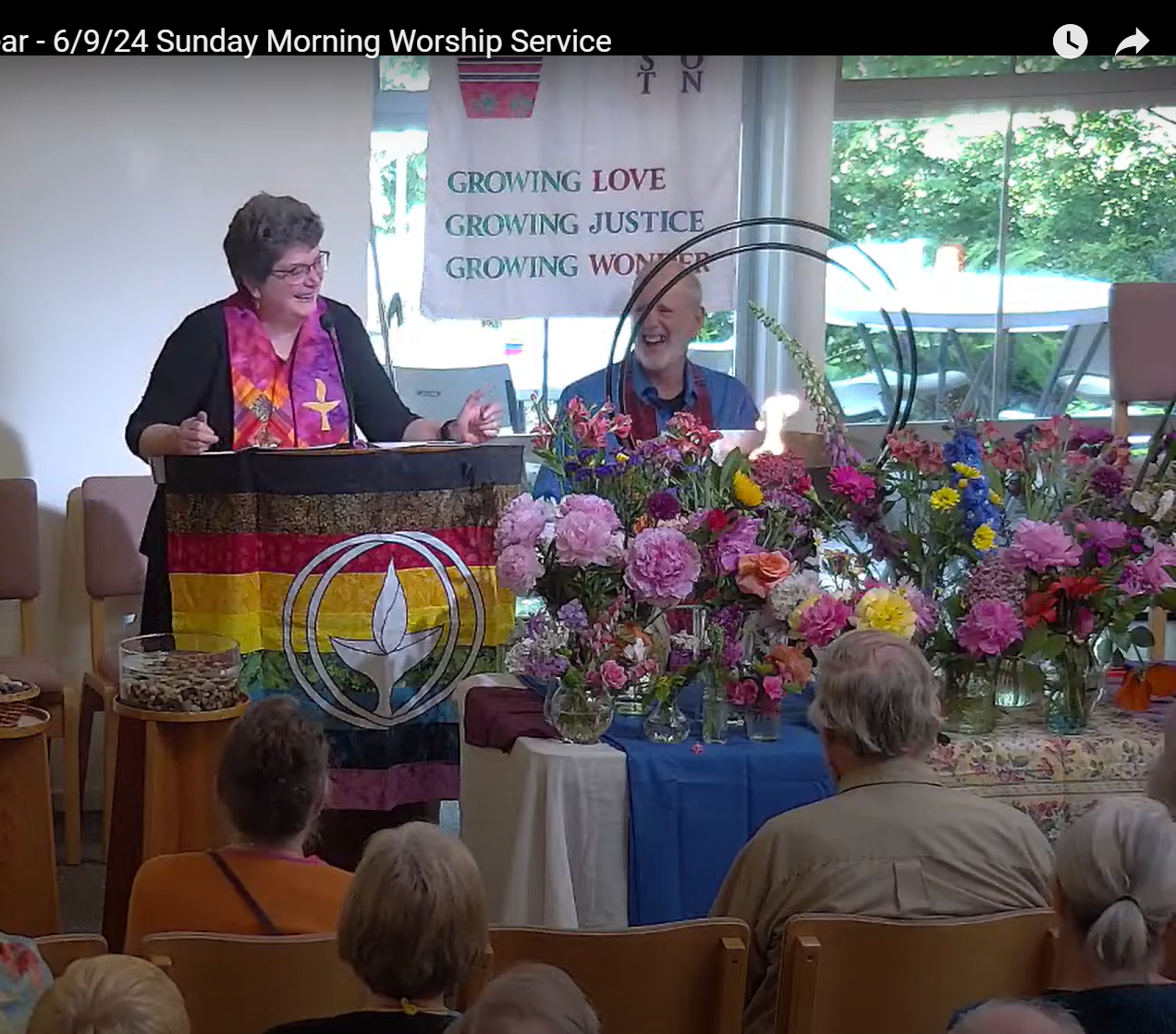 Rev. Mary laughing at the pulpit on Flower Communion Sunday as she tells the story of how she learned the real meaning of the song Run Mary Run